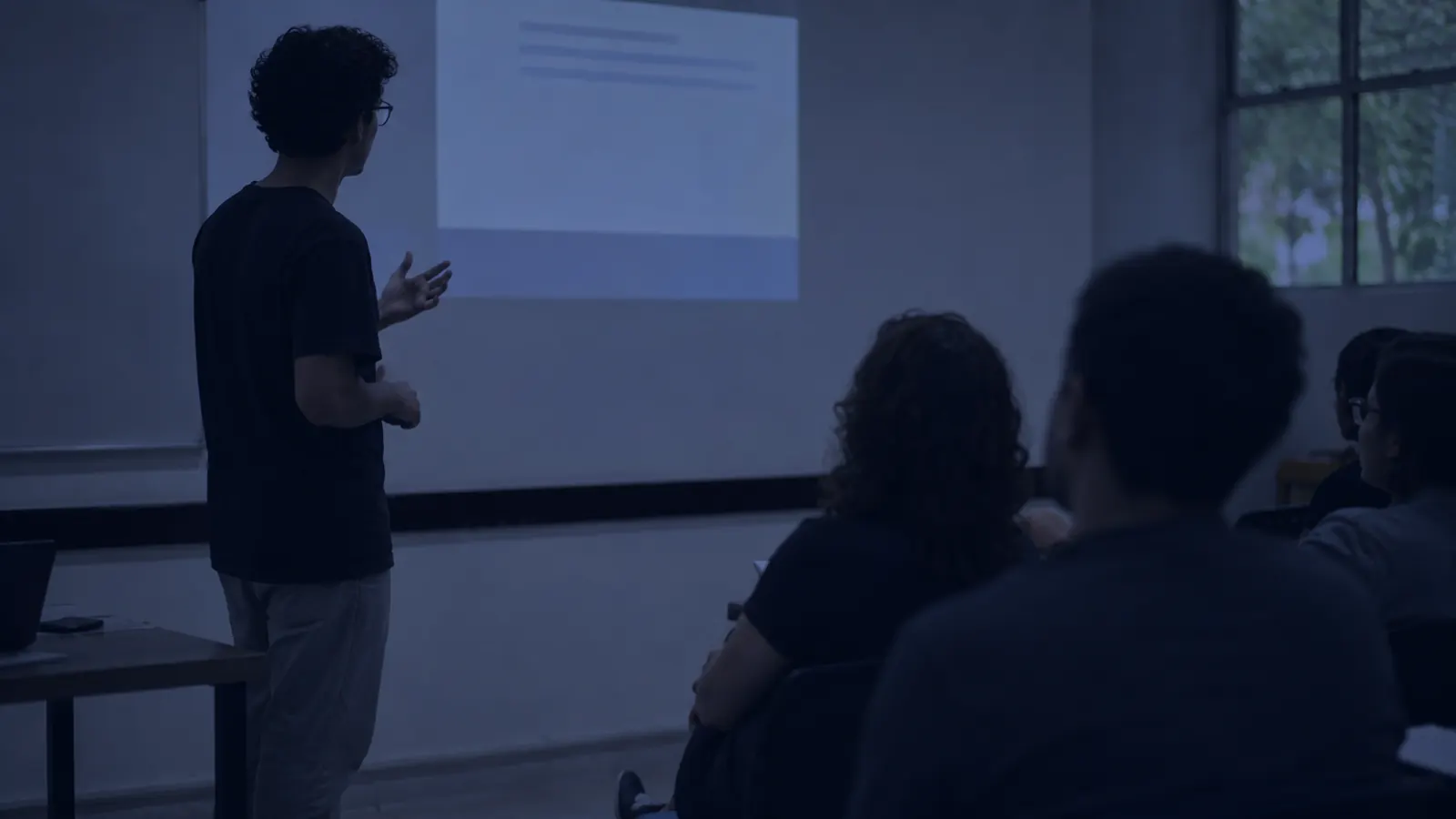 Estudante apresentando um trabalho a um pequeno grupo em sala de aula.